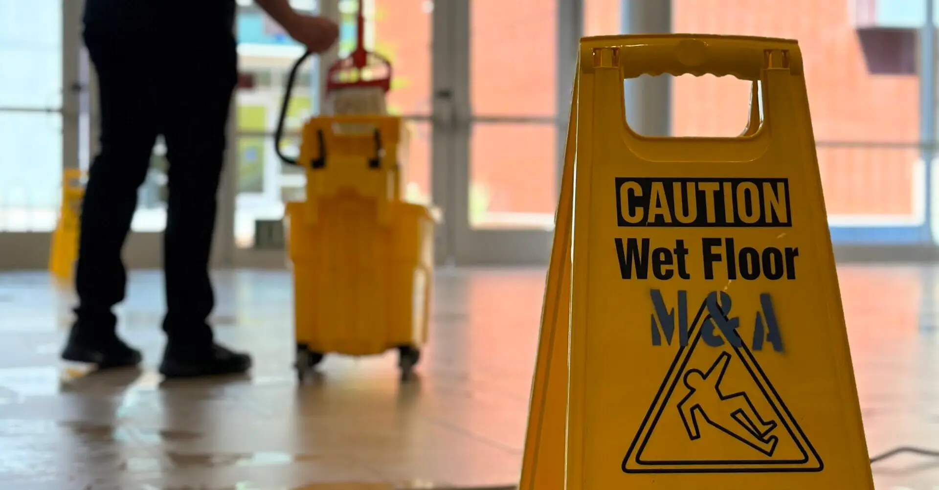 caution wet floor sign in the foreground with a person mopping in the background