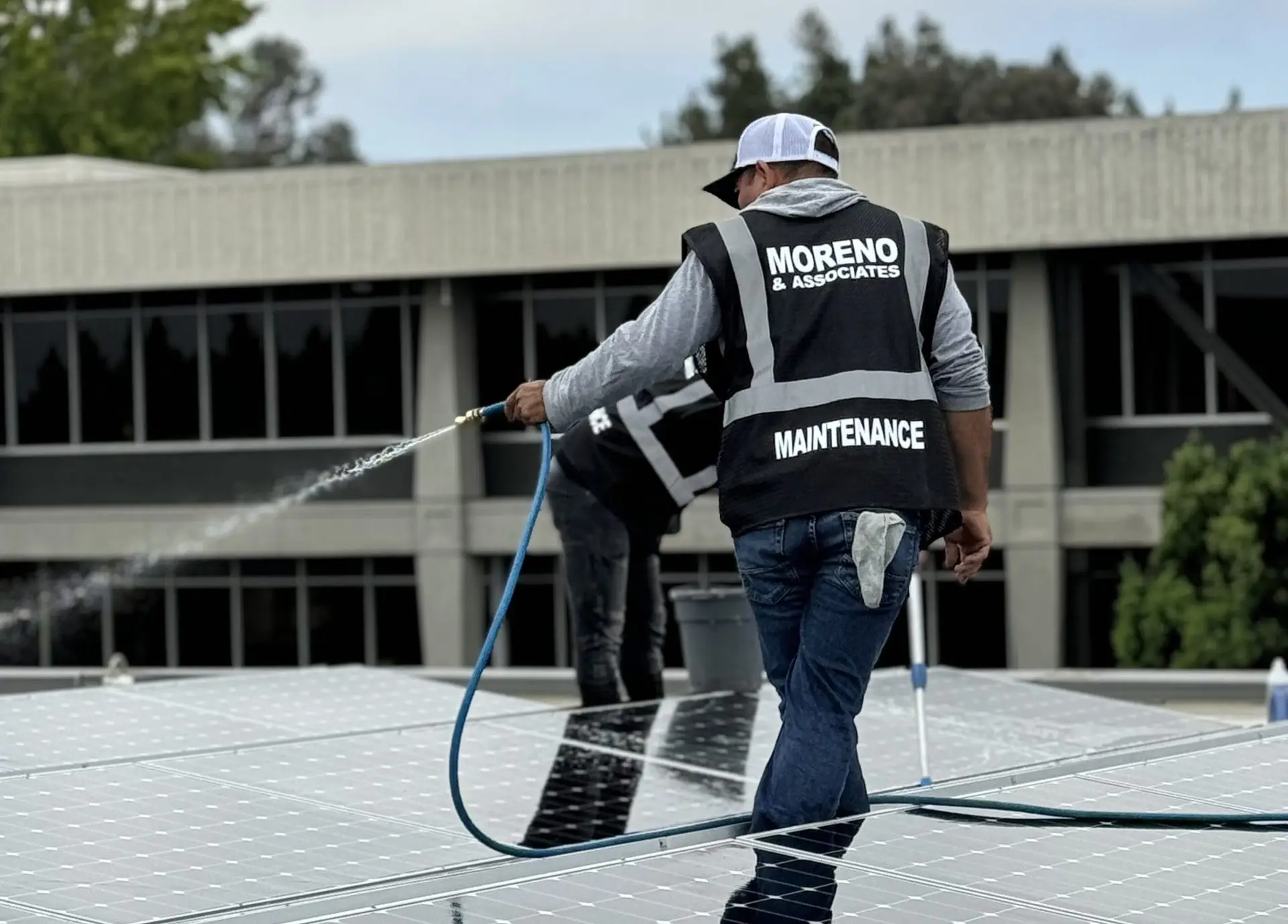 moreno utility crew with back turned towards camera holding a hose that is being used to pressure wash solar panels on top of a roof.